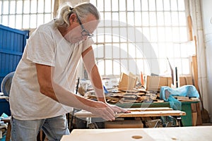 Senior carpenter working on wood craft at workshop producing wooden furniture.