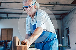Senior carpenter working with wood planer on workpiece
