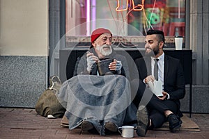 Senior caucasian beggar male telling story about life to businessman