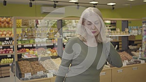 Senior Caucasian blond woman choosing purchases in grocery. Portrait of housewife buying products in supermarket. Retail