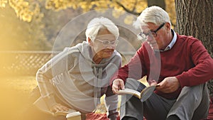 Senior Caucasian couple having picnic reading a book in the park medium shot selective focus