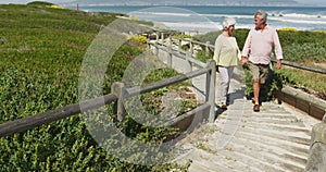 Senior caucasian couple holding hands and walking on path leading to the beach