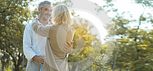 Senior Caucasian couple hugging in park. Family with a happy smile feels relaxed with nature in the morning. Or in the evening. En