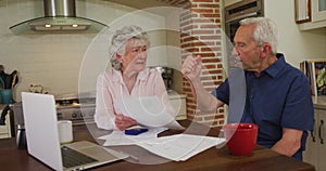 Senior caucasian couple sitting in kitchen checking paperwork