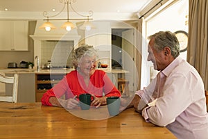 Senior caucasian couple sitting at table together drinking coffee in kitchen