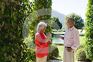 Senior caucasian couple smiling and holding mugs in sunny garden
