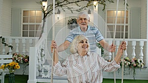 Senior couple together in front yard at home. Man swinging and hugging woman. Happy mature family