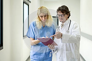 Senior caucasian doctor having discussion in a hospital hallway with nurse. Team of doctors working together on patients file at