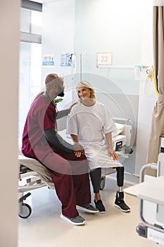 Senior caucasian female patient with prosthetic leg and african american male doctor sitting on bed