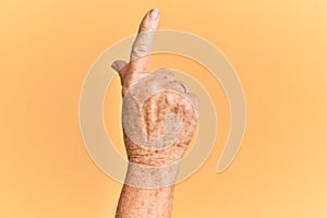 Senior caucasian hand over yellow isolated background counting number one using index finger, showing idea and understanding