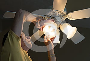Senior caucasian man dusting lamp shade in ceiling fan and light