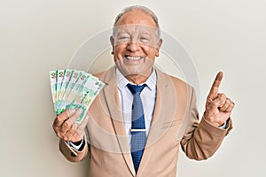 Senior caucasian man holding 50 hong kong dollars banknotes smiling with an idea or question pointing finger with happy face,