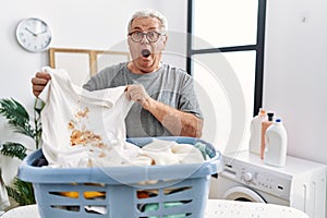 Senior caucasian man holding dirty t shirt with stain celebrating crazy and amazed for success with open eyes screaming excited