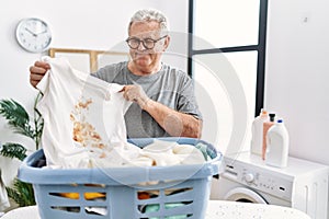 Senior caucasian man holding dirty t shirt with stain smiling with a happy and cool smile on face