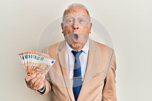 Senior caucasian man holding euro banknotes scared and amazed with open mouth for surprise, disbelief face