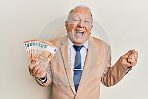 Senior caucasian man holding euro banknotes screaming proud, celebrating victory and success very excited with raised arm