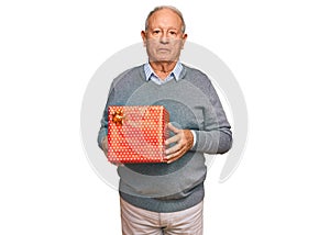 Senior caucasian man holding gift thinking attitude and sober expression looking self confident