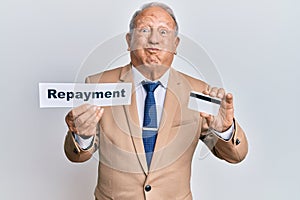 Senior caucasian man holding payment word paper and credit card puffing cheeks with funny face