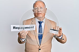 Senior caucasian man holding payment word paper and credit card relaxed with serious expression on face