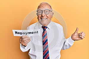 Senior caucasian man holding repayment word paper screaming proud, celebrating victory and success very excited with raised arm