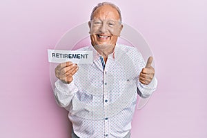 Senior caucasian man holding retirement word paper smiling happy and positive, thumb up doing excellent and approval sign
