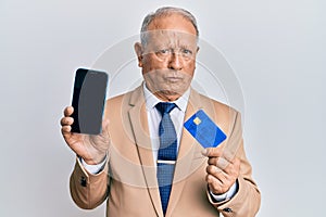 Senior caucasian man holding smartphone and credit card skeptic and nervous, frowning upset because of problem