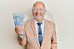 Senior caucasian man holding south african 20 rand banknotes looking positive and happy standing and smiling with a confident