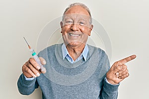 Senior caucasian man holding syringe smiling happy pointing with hand and finger to the side