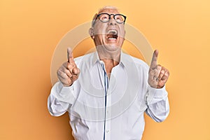 Senior caucasian man pointing up with fingers angry and mad screaming frustrated and furious, shouting with anger looking up