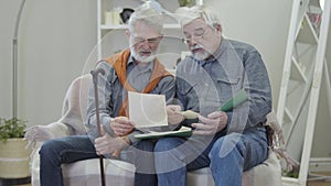 Senior Caucasian man showing old black and white photos to friend in nursing home. Two positive mature retirees in