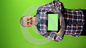 Senior caucasian man showing tablet with horizontal green screen and smiling.