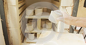 Senior caucasian man wearing apron firing pots in kiln at pottery workshop