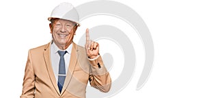 Senior caucasian man wearing architect hardhat pointing finger up with successful idea