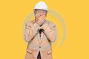 Senior caucasian man wearing architect hardhat shocked covering mouth with hands for mistake