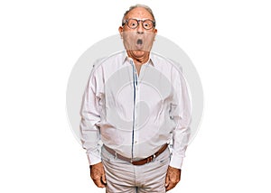 Senior caucasian man wearing business shirt and glasses afraid and shocked with surprise expression, fear and excited face
