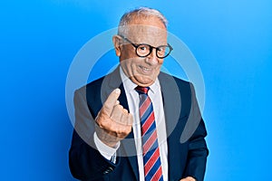 Senior caucasian man wearing business suit and tie beckoning come here gesture with hand inviting welcoming happy and smiling