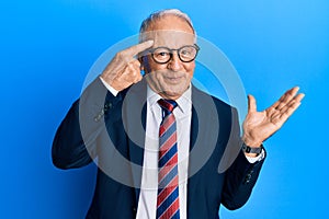 Senior caucasian man wearing business suit and tie confused and annoyed with open palm showing copy space and pointing finger to