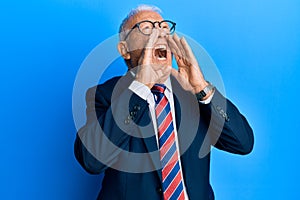 Senior caucasian man wearing business suit and tie shouting angry out loud with hands over mouth