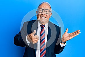 Senior caucasian man wearing business suit and tie showing palm hand and doing ok gesture with thumbs up, smiling happy and