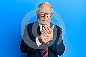 Senior caucasian man wearing business suit and tie suffering pain on hands and fingers, arthritis inflammation