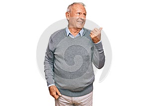 Senior caucasian man wearing casual clothes smiling with happy face looking and pointing to the side with thumb up