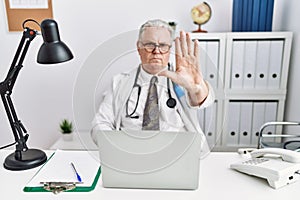 Senior caucasian man wearing doctor uniform and stethoscope at the clinic doing stop sing with palm of the hand