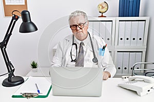 Senior caucasian man wearing doctor uniform and stethoscope at the clinic looking sleepy and tired, exhausted for fatigue and