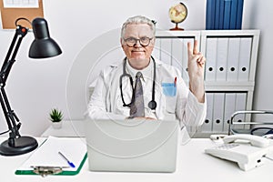 Senior caucasian man wearing doctor uniform and stethoscope at the clinic smiling with happy face winking at the camera doing