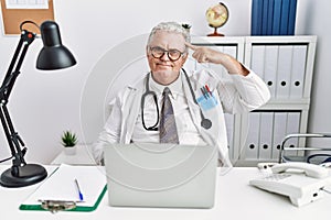 Senior caucasian man wearing doctor uniform and stethoscope at the clinic smiling pointing to head with one finger, great idea or