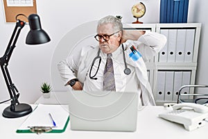 Senior caucasian man wearing doctor uniform and stethoscope at the clinic suffering of neck ache injury, touching neck with hand,