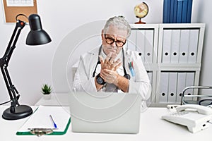 Senior caucasian man wearing doctor uniform and stethoscope at the clinic suffering pain on hands and fingers, arthritis