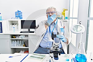Senior caucasian man working at scientist laboratory shocked covering mouth with hands for mistake