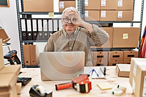 Senior caucasian man working at small business ecommerce with laptop doing ok gesture with hand smiling, eye looking through