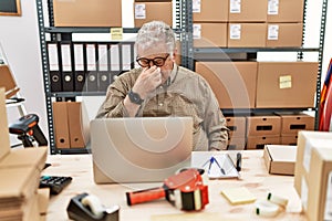 Senior caucasian man working at small business ecommerce with laptop tired rubbing nose and eyes feeling fatigue and headache